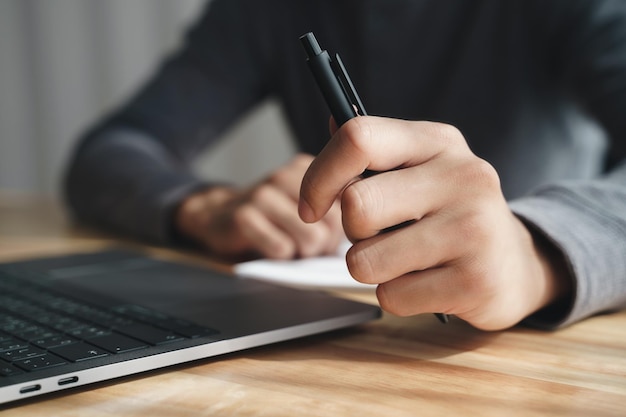 Empresario sosteniendo un bolígrafo con la mano izquierda trabajando con una laptop en la oficina