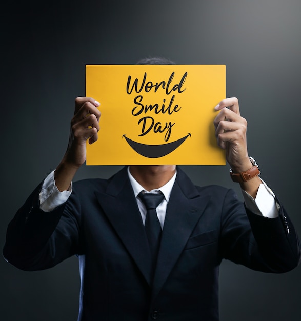 Empresario sosteniendo un cartel amarillo del día mundial de la sonrisa