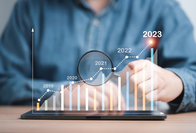 Empresario sosteniendo una lupa para encontrar un gráfico técnico virtual en aumento y una flecha hacia arriba para el análisis de comerciantes para buscar el mejor crecimiento comercial y el retorno de ganancias del concepto de gráfico del mercado de valores