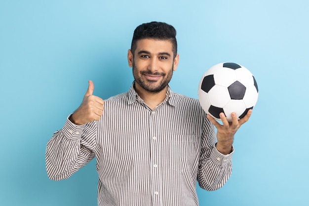 Empresario sosteniendo una pelota de fútbol en su mano con una expresión positiva sonriente mostrando el pulgar hacia arriba