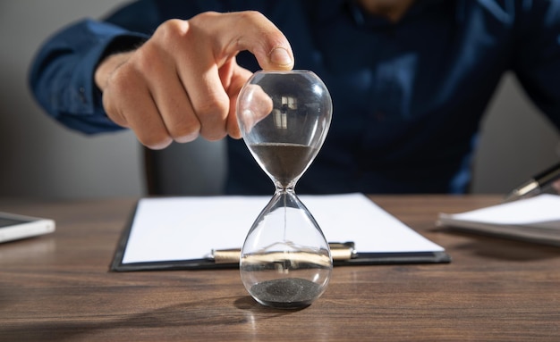 Foto empresario sosteniendo reloj de arena sobre la mesa