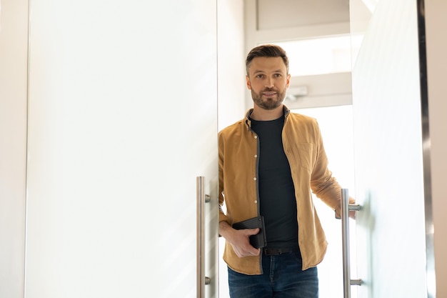 Empresario sosteniendo una tableta abriendo una puerta de vidrio y entrando en una oficina moderna