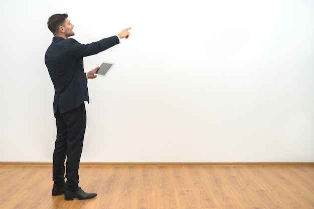 El empresario sosteniendo una tableta y gesticulando sobre el fondo de la pared blanca