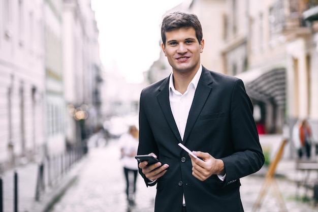 Empresario sosteniendo una tarjeta de crédito y haciendo pagos en línea en su teléfono móvil hombre feliz de pie en la calle de la ciudad