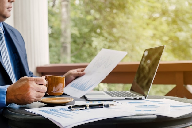 Empresario sosteniendo la taza de café analizar el gráfico con el portátil en la oficina en casa