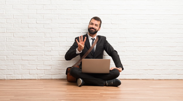 Empresario con su laptop sentada en el piso feliz y contando cuatro con los dedos