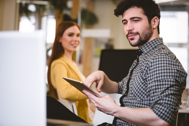 Empresario con tableta digital con compañero de trabajo en segundo plano.