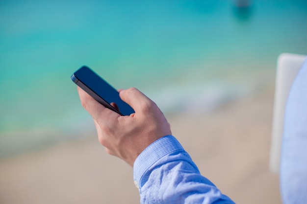 Empresario con teléfono en mano en una playa tropical