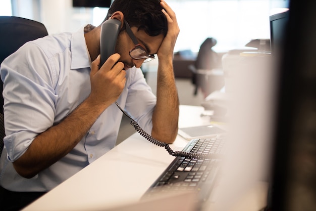 Empresário tenso falando por telefone fixo no escritório