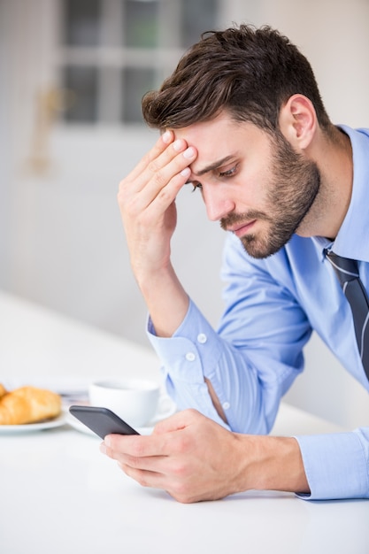 Empresario tenso usando el teléfono móvil por mesa