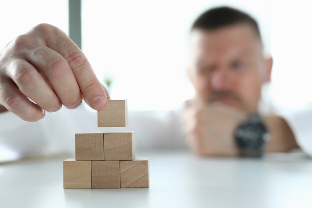 Foto el empresario tiene cubos de madera en sus manos y construye una pirámide.