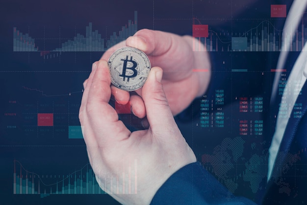 El empresario tiene una moneda bitcoin de oro en sus manos. El panel de información holográfica con estadísticas muestra la caída y el crecimiento de la criptomoneda. Concepto de moneda virtual y blockchain.