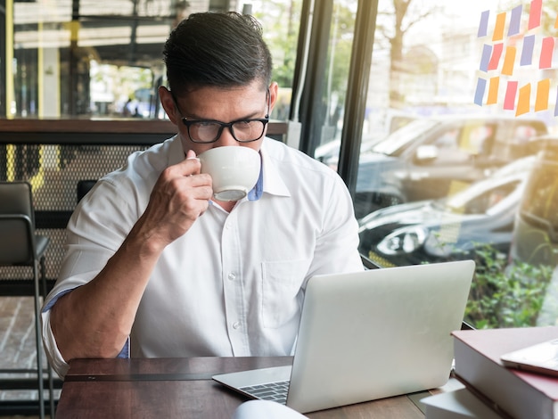 Empresario tomando café o té mientras usa la computadora portátil en una cafetería