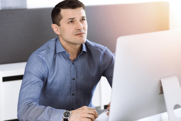 Empresario trabajando con computadora en una oficina moderna y soleada. Captura de cabeza de empresario masculino o director de empresa en el lugar de trabajo. Concepto de negocio.