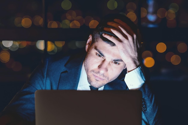 Empresario trabajando en una computadora portátil pensando sentado en la oficina por la noche