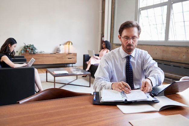 Empresario trabajando en escritorio colegas femeninas en segundo plano.