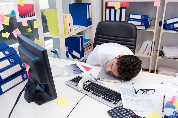 Empresario trabajando en la oficina con montones de libros y papeles