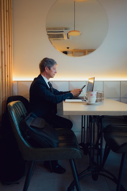 Foto empresario trabajando remotamente en una cafetería mirando su teléfono móvil