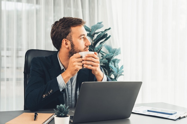 Empresario trabajando en su computadora portátil y tomando café en su escritorio Entidad
