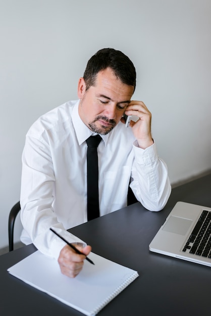 Empresario trabajando en el teléfono y escribiendo notas sentado en un escritorio en la oficina