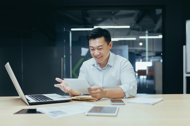 Empresario en el trabajo hombre asiático leyendo una buena carta del banco sobre la apertura de una línea de crédito