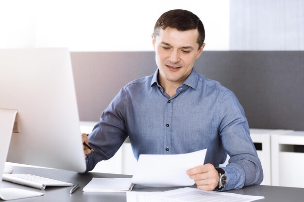 Empresário trabalhando com computador no escritório ensolarado moderno. Tiro na cabeça do empresário masculino ou diretor da empresa no local de trabalho. Conceito de negócios.