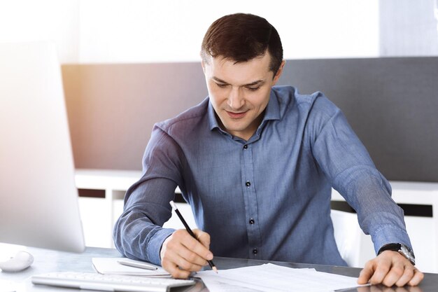 Empresário trabalhando com computador no escritório ensolarado moderno. Tiro na cabeça do empresário masculino ou diretor da empresa no local de trabalho. Conceito de negócios.