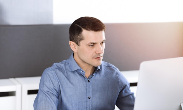 Empresário trabalhando com computador no escritório moderno e ensolarado. Tiro na cabeça do empresário masculino ou diretor da empresa no local de trabalho. Conceito de negócios.