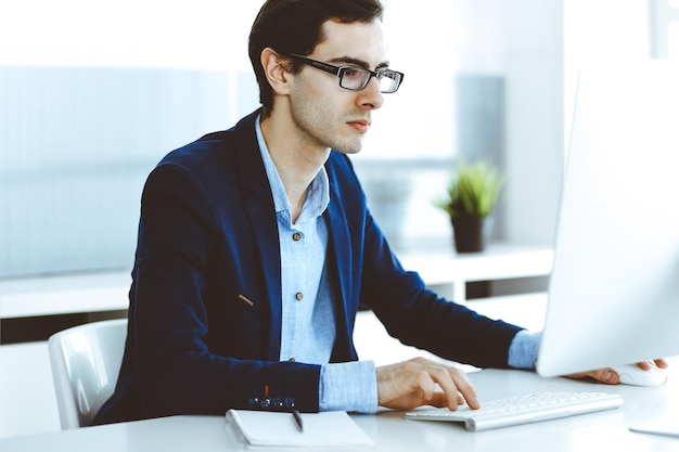 Empresário trabalhando com computador no escritório moderno. Tiro na cabeça do empresário masculino ou gerente da empresa no local de trabalho. Conceito de negócios.