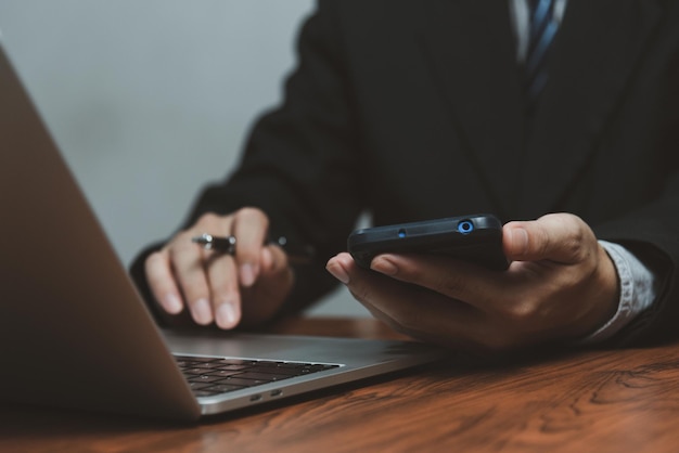 Empresário trabalhando com smartphone nas mãos e computador portátil na mesa