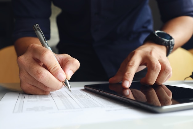 Empresário trabalhando no escritório, ele está usando o touchpad, lendo um e-mail no tablet e fazendo anotações no papel