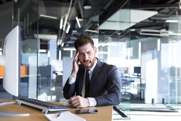 Foto empresário trabalhando no escritório em uma mesa com um computador um homem cansado tem uma forte dor de cabeça