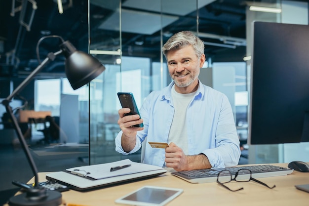 Empresário trabalhando no escritório marido fazendo compras on-line usando telefone e gerente de aplicativos móveis segurando cartão de banco de crédito