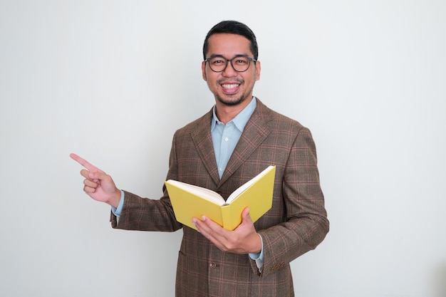 Empresario con traje marrón y sosteniendo un libro sonriendo mientras señala con el dedo hacia el lado derecho