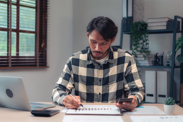 Foto empresário usa smartphone e faz anotações em papel enquanto verifica relatório financeiro e contábil