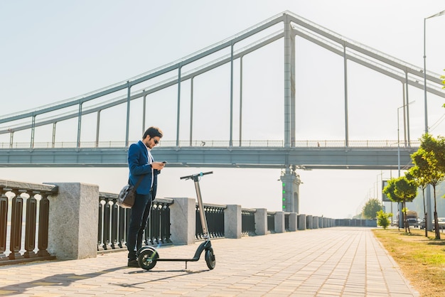 Empresário usando celular enquanto parado na scooter elétrica na rua da cidade