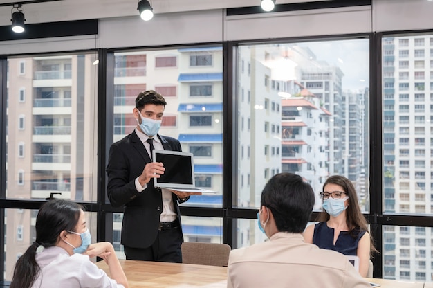 Empresário usando máscara facial com apresentação de plano de negócios no laptop. Reunião de negócios corporativos em um escritório moderno