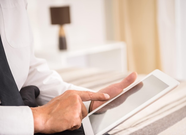 Empresario usando su tableta digital mientras está sentado en la cama en la habitación del hotel Closeup