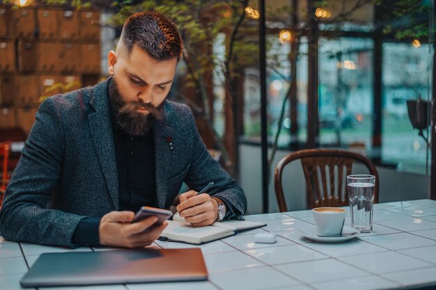 Empresario usando un teléfono inteligente y una computadora portátil en un café