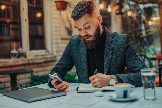 Empresario usando un teléfono inteligente y una computadora portátil en una cafetería