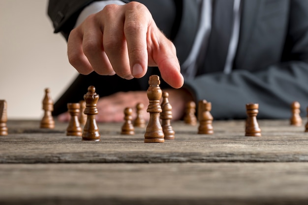 Empresário, vestindo terno de negócio, jogando uma partida de xadrez em uma velha mesa de madeira em um close-up vista de sua mão alcançando o pedaço rei preto.