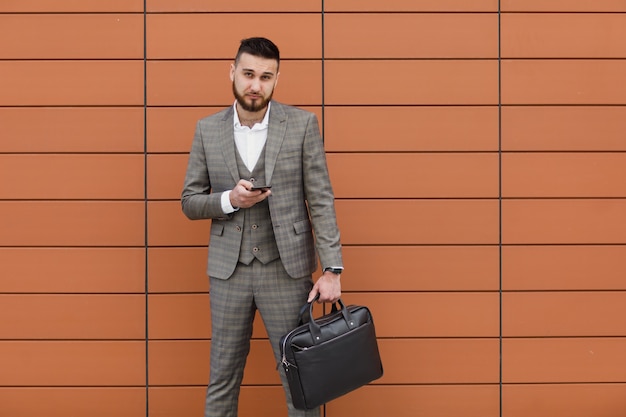 Empresário vestindo terno e usando smartphone moderno perto do escritório no início da manhã, empregador bem-sucedido para fazer um acordo perto de um arranha-céu