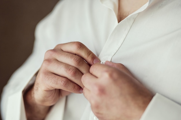 El empresario viste camisa blanca, primer plano de manos masculinas, novio preparándose en la mañana antes de la ceremonia de boda