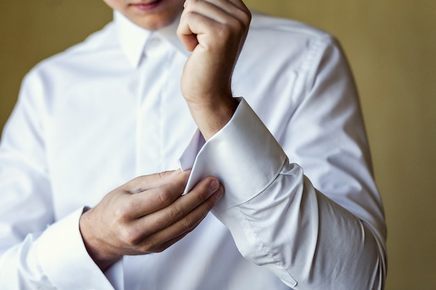 El empresario viste camisa blanca, primer plano de manos masculinas, novio preparándose en la mañana antes de la ceremonia de boda