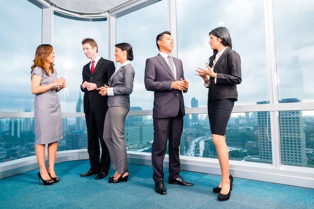 Empresários asiáticos em pé e conversando em frente à janela do escritório