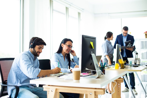 Foto empresários atraentes com fones de ouvido sorrindo enquanto trabalham com o computador em um escritório moderno