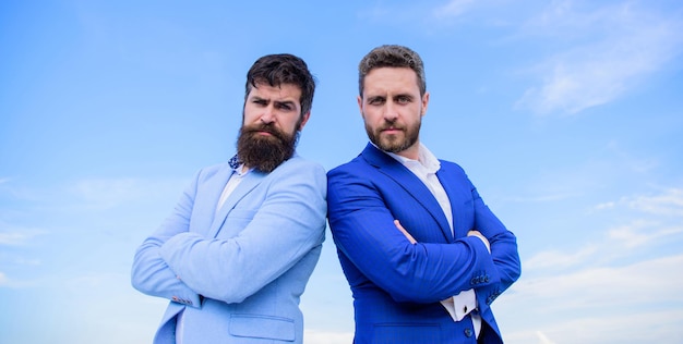 Empresários barbudos posando com confiança. Homens de negócios ficam o fundo do céu azul. Perfeito em cada detalhe. A aparência bem cuidada melhora a reputação do empresário. Conceito de pessoas de negócios.