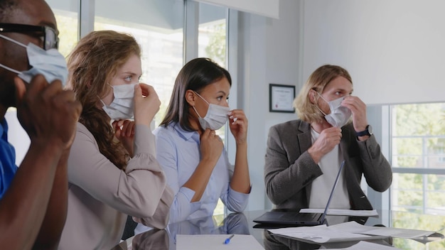 Empresários com máscara facial sentados à mesa durante reunião corporativa em escritório moderno