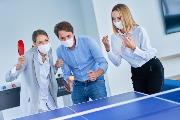 empresários com máscaras protetoras jogando tênis de mesa em um escritório compartilhado