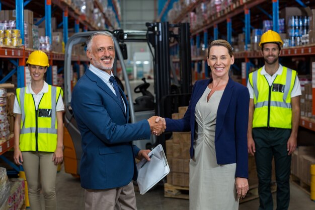 Los empresarios se dan la mano y miran la cámara frente a los trabajadores